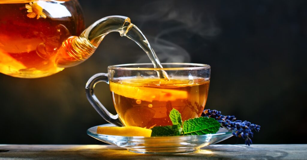 Hot herbal tea being poured into a clear glass cup