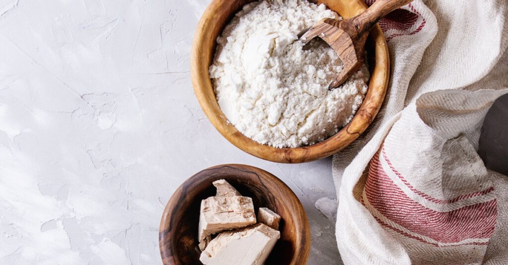 Wooden bowls with flour and fresh yeast on a kitchen counter